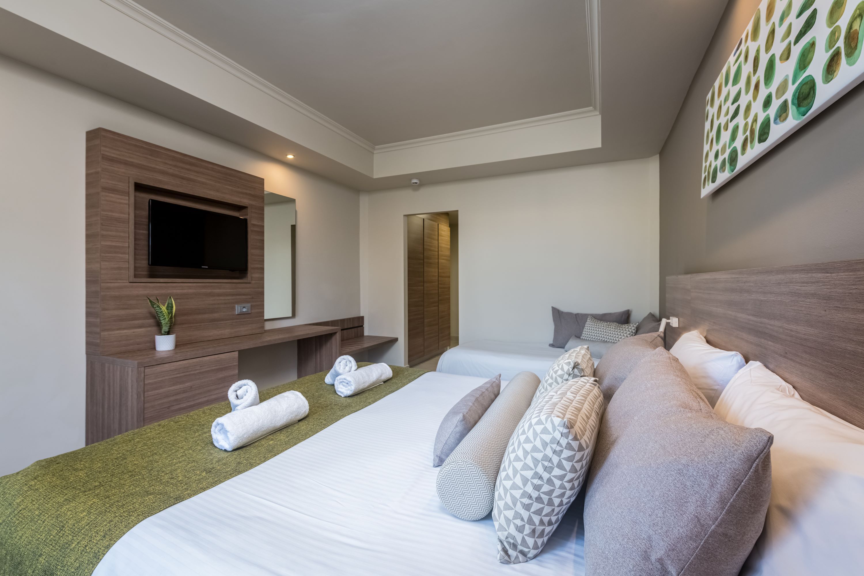 A hotel room with a large bed, a flat-screen TV, a wooden dresser, and a painting on the wall.