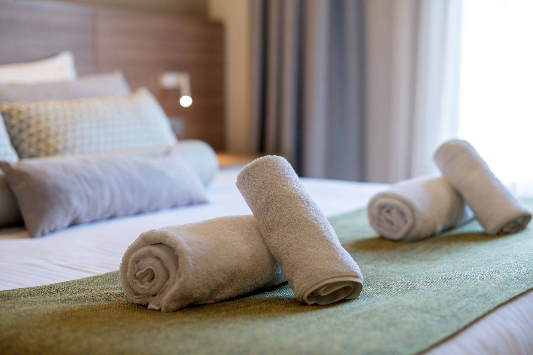 Cama bem arrumada com toalhas dobradas e um espalha cama verde.