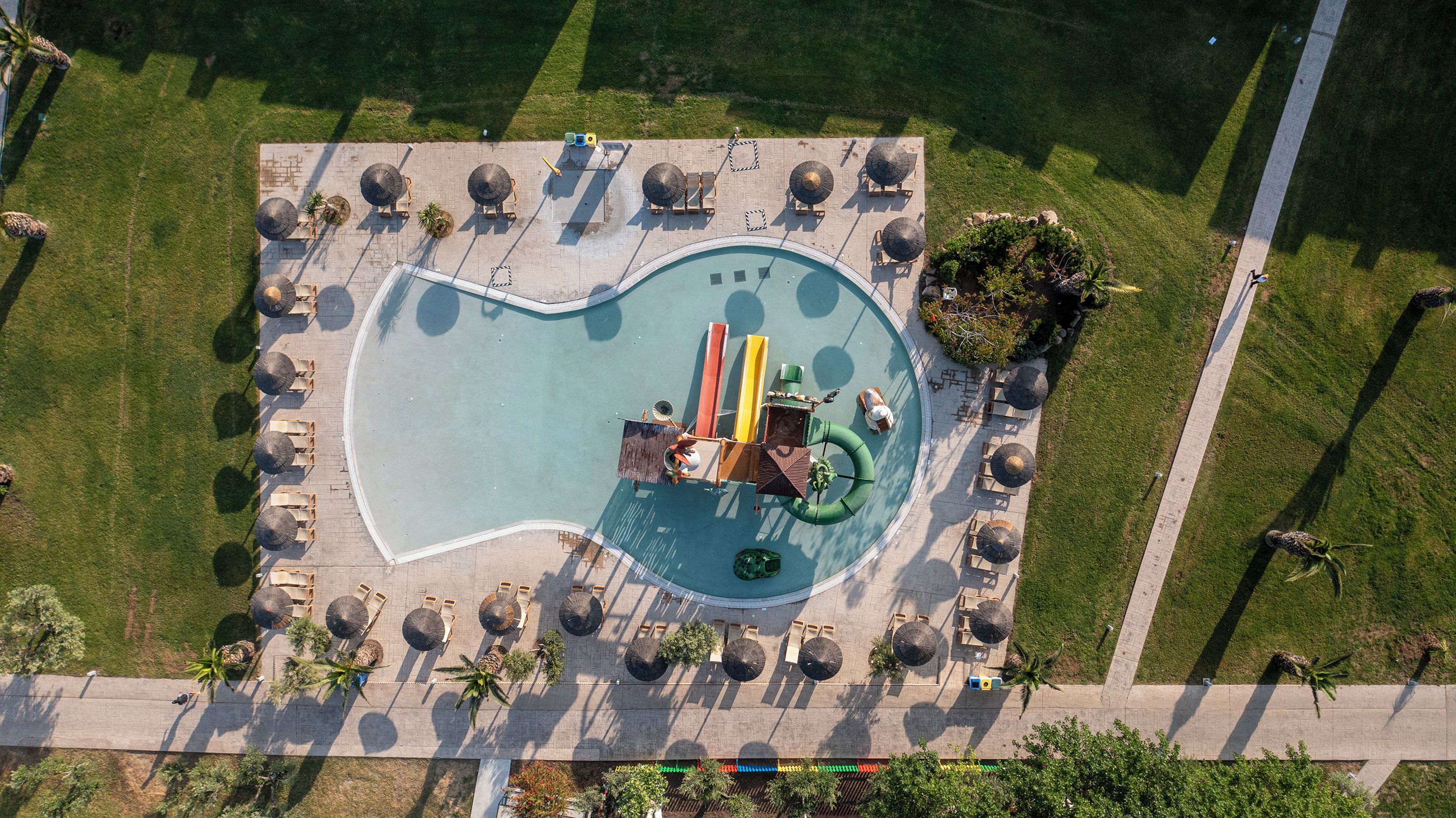 An aerial view of a swimming pool with a heart-shaped design, surrounded by lounge chairs and umbrellas.