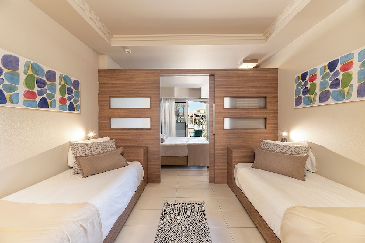 Habitación de hotel con dos camas, vistas a través de un ventanal y arte abstracto en las paredes.