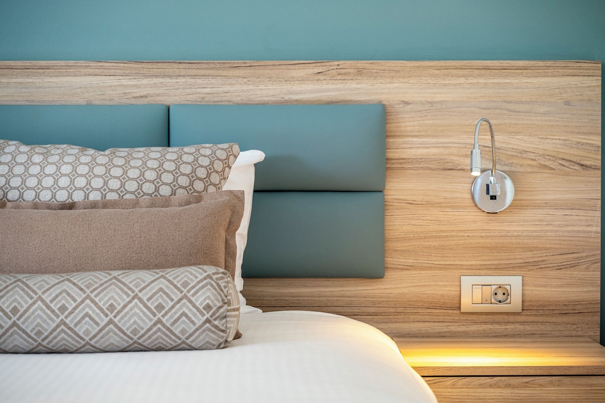 Una cama bien hecha con almohadas estampadas, un cabecero de madera y un aplique de pared.