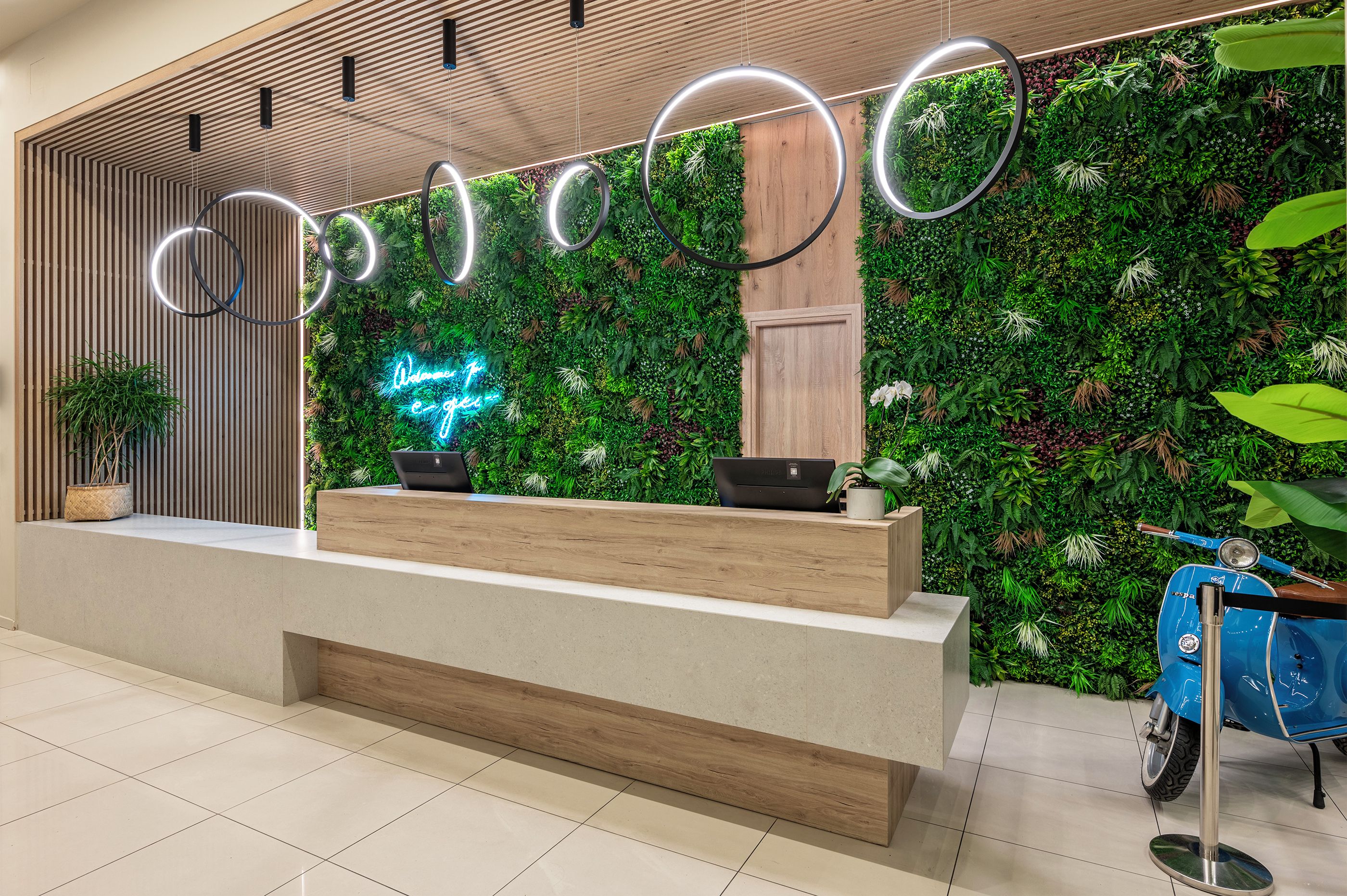 Un mostrador de recepción con detalles de madera, un letrero de neón y una pared verde decorada con plantas.