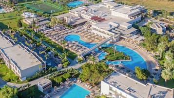 Vista aérea de un resort con varias piscinas, tumbonas y palmeras.