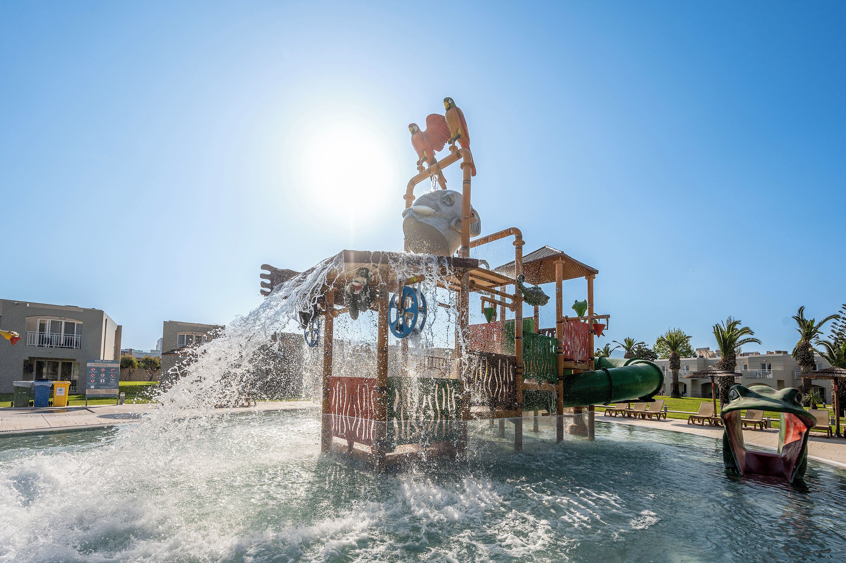Una fuente de agua con una escultura de pájaro, rodeada por una piscina y edificios al fondo.