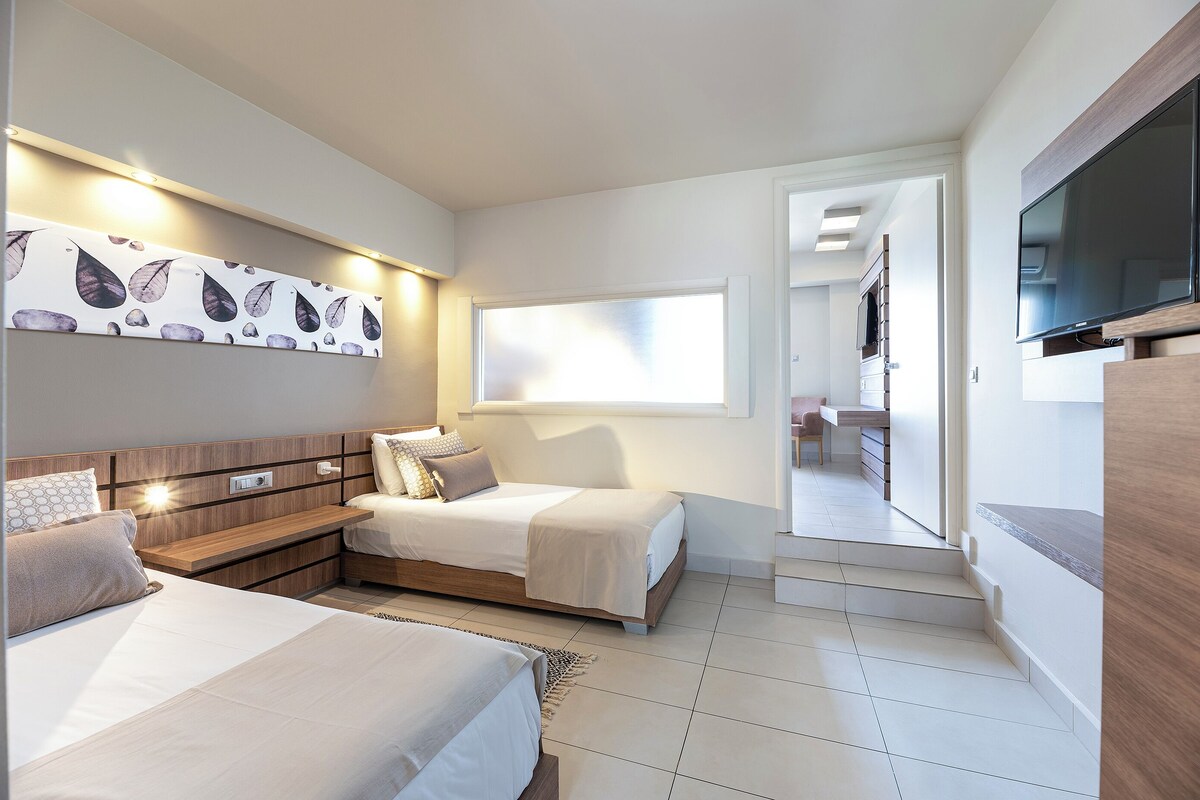 Ein modernes Hotelzimmer mit zwei Betten, einem Flachbildfernseher, einem großen Fenster und Blick auf den Flur.