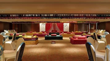 A spacious hall with tiered seating, a stage with red drapery, and a patterned carpet.
