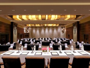 Un salón de conferencias con varias mesas redondas, sillas blancas y un techo alto con iluminación empotrada.