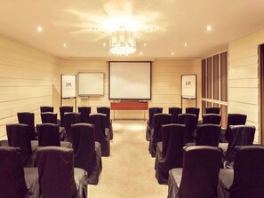 Une salle de conférence avec des rangées de chaises, un écran de projection et deux tableaux blancs.