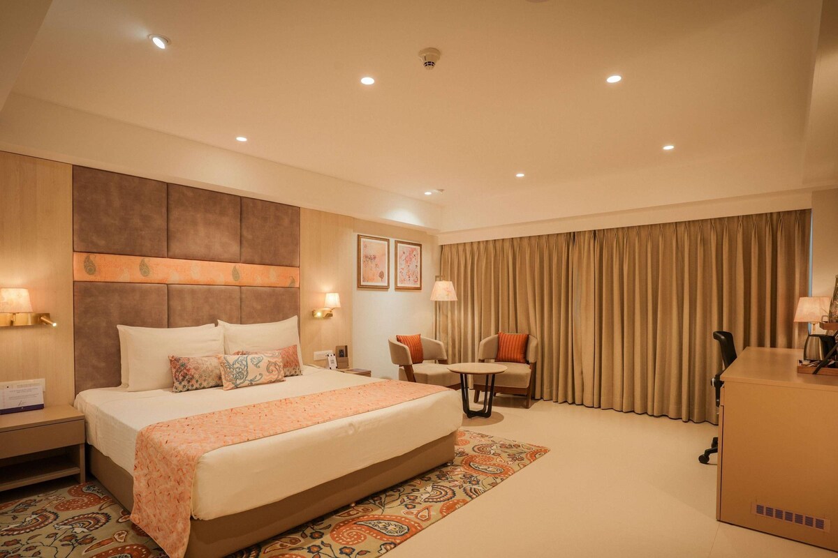 A hotel room with a large bed, two armchairs, a small table, and a desk.