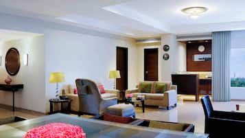 A modern hotel room with a glass dining table, two sofas, a coffee table, a lamp, and a view of the city.