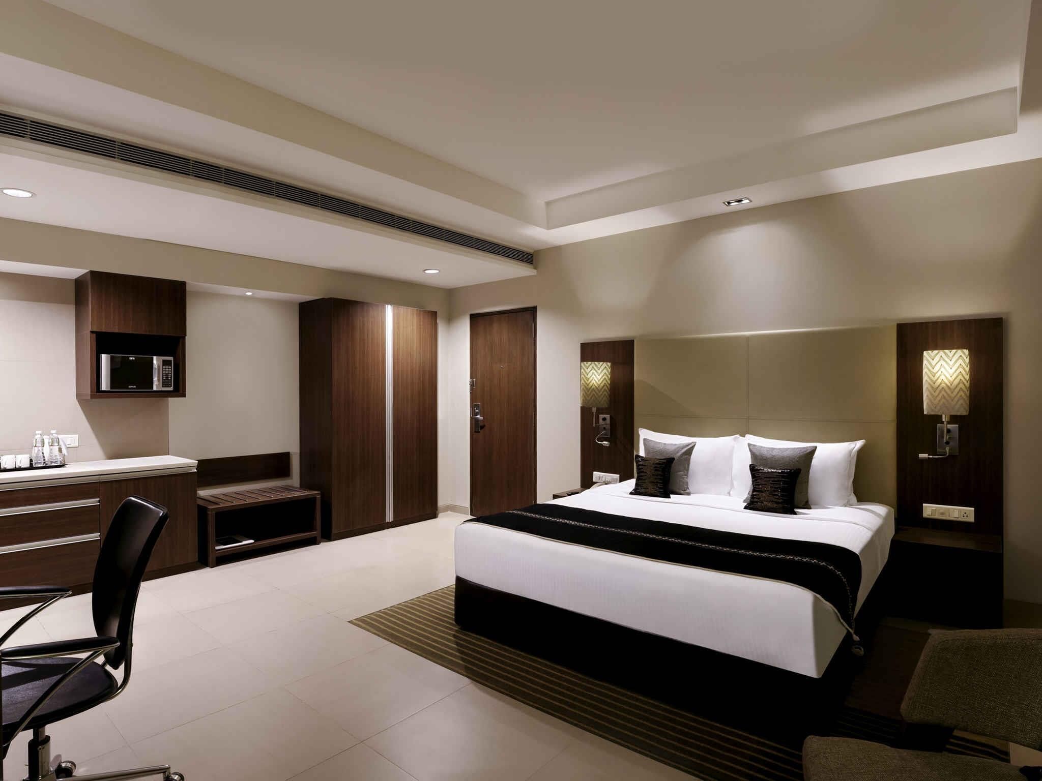 Una habitación de hotel moderna con cama, escritorio, silla, armario e iluminación integrada.