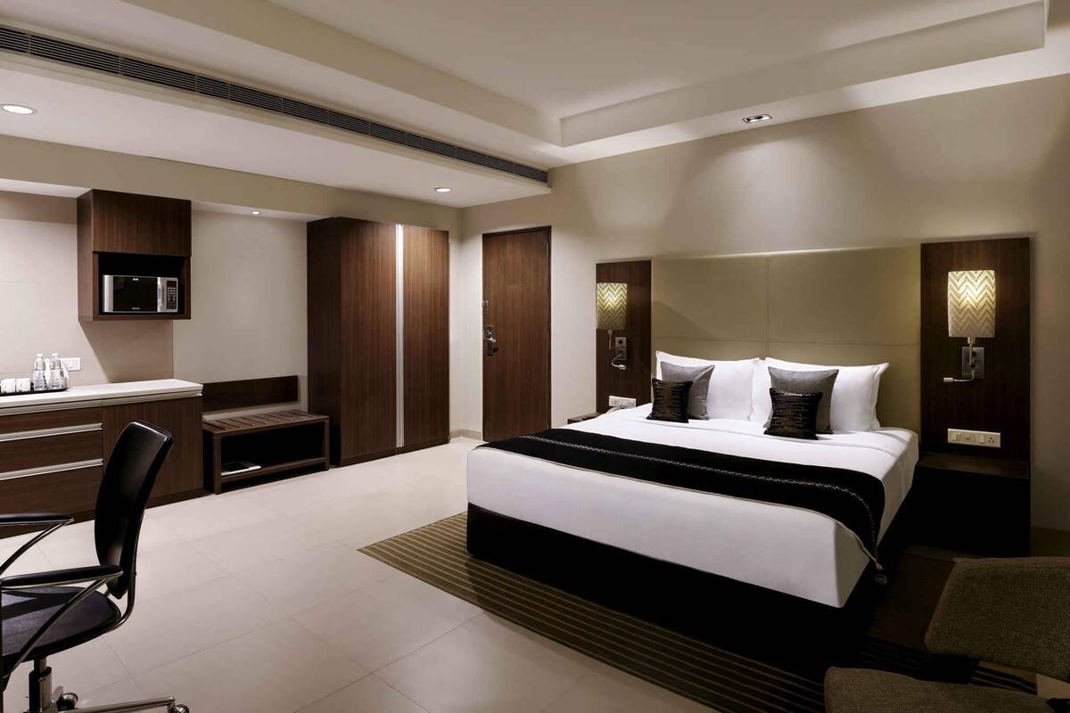 Ein modernes Hotelzimmer mit Bett, Schreibtisch, Stuhl, Kleiderschrank und integrierter Beleuchtung.