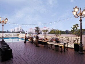 Un área de piscina en la azotea con bar, sillones de descanso y luces colgantes.