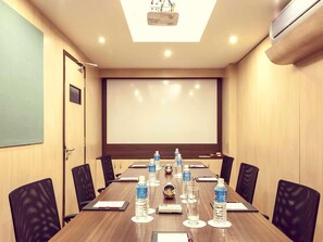 Un salón de conferencias con una larga mesa, sillas, botellas de agua, un proyector y una pantalla.