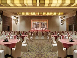 A banquet hall with round tables, white chairs, and a stage with floral decorations. - Grand Mercure Vadodara Surya Palace (Vadodara)