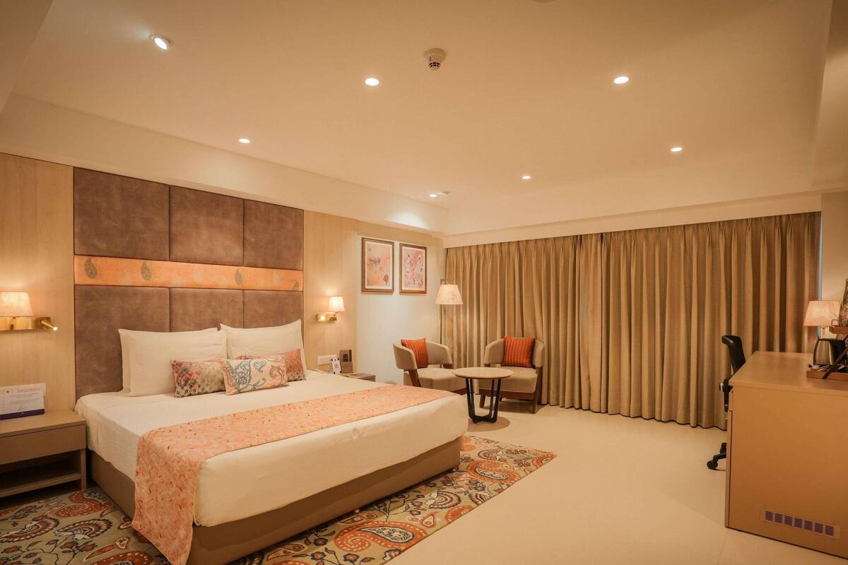 Ein Hotelzimmer mit einem großen Bett, zwei Sesseln, einem kleinen Tisch und einem Schreibtisch.