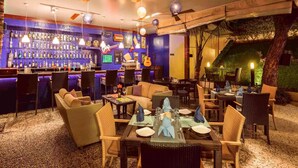 A bar area with a variety of bottles, a seating area with tables and chairs, and a view of the outdoors. - Grand Mercure Vadodara Surya Palace (Vadodara)