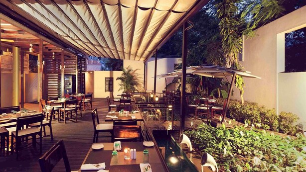 An outdoor dining area with tables and chairs, a covered seating area, and a water feature. - Grand Mercure Vadodara Surya Palace (Vadodara)