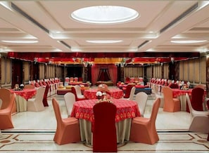 A banquet hall with round tables and chairs, a stage with curtains, and a chandelier.