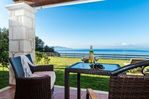 Un patio con mobili in vimini, un tavolo in vetro e una bottiglia di vino.