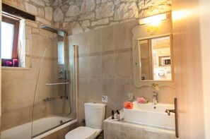 Un bagno con parete in pietra, box doccia in vetro, WC bianco e lavabo con specchio.