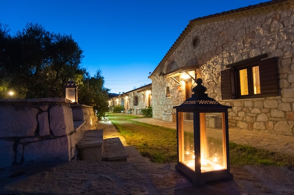 A stone building with a stone pathway leading to the entrance, a lantern, and a well-lit interior.