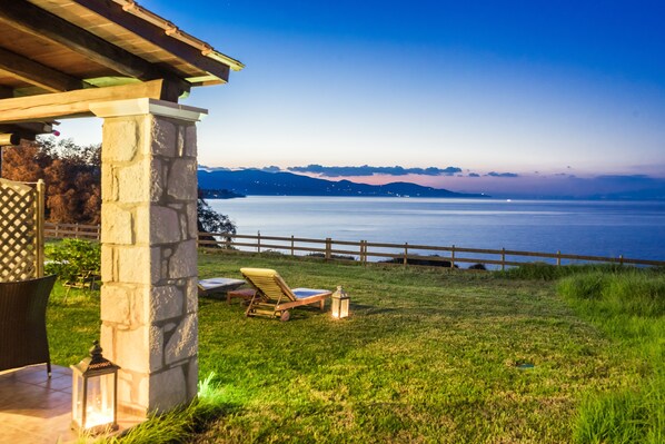 Un patio con un pilastro in pietra, una recinzione di legno e vista su un corpo d'acqua con montagne sullo sfondo.