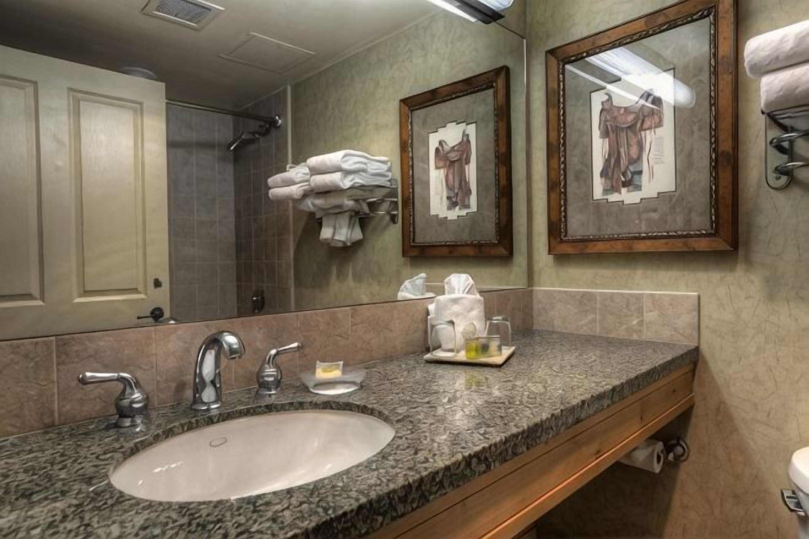 A bathroom with a sink, mirrors, towels, and a framed picture on the wall.