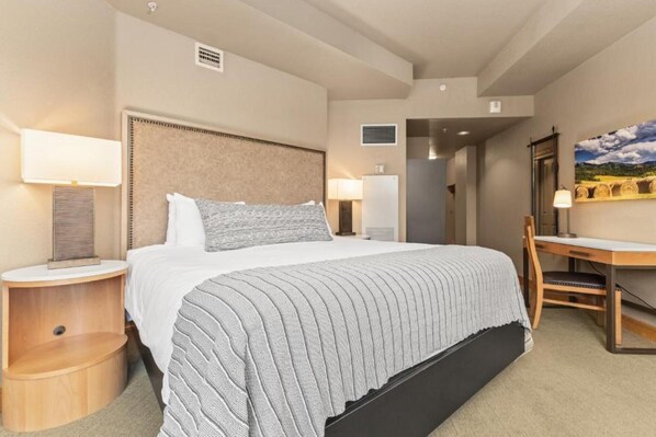 A hotel room with a large bed, two bedside tables with lamps, a desk, and a chair. - The Steamboat Grand (Steamboat Springs)