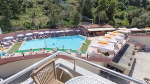 A pool area with multiple lounge chairs and umbrellas, surrounded by trees.