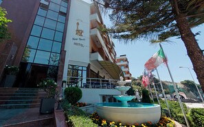 Un hotel con una fuente, escalones que conducen a la entrada y banderas.