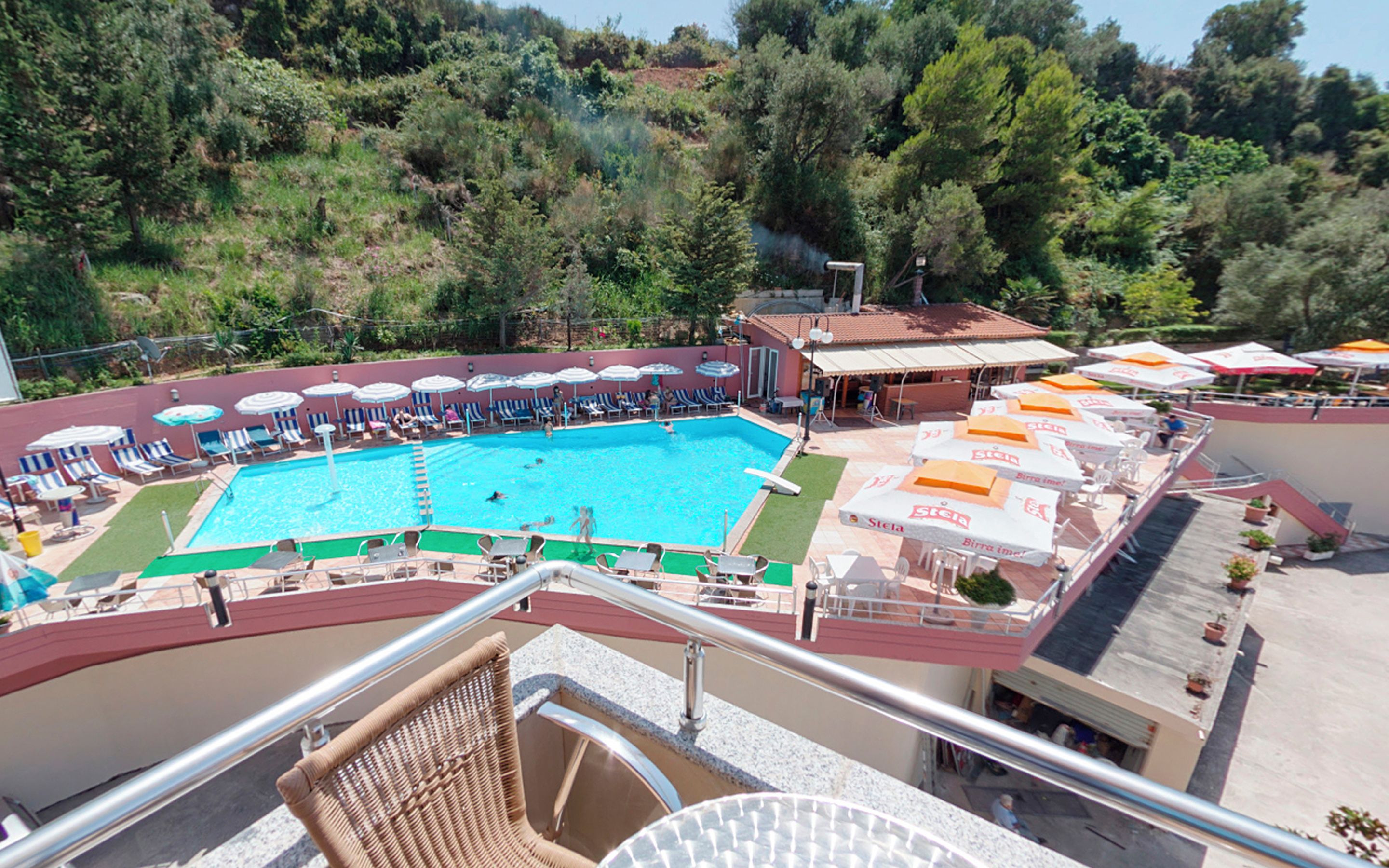 A swimming pool with lounge chairs and umbrellas, surrounded by trees and a building with outdoor seating.