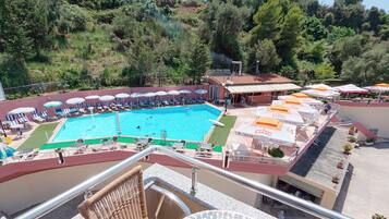 A swimming pool with lounge chairs and umbrellas, surrounded by trees and a building with outdoor seating.