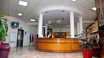 A reception area with a wooden reception desk, a television mounted on the wall, and several flags.