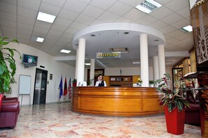Un área de recepción con un mostrador de madera, un televisor montado en la pared y varias banderas.