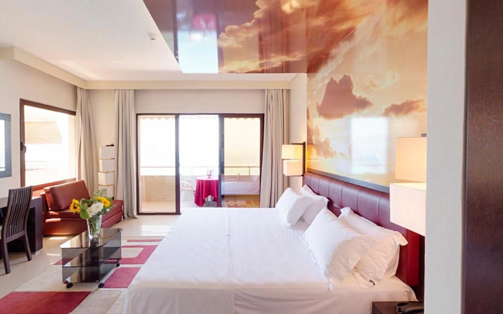 A hotel room with a large bed, a sofa, a desk, and a balcony with a view.