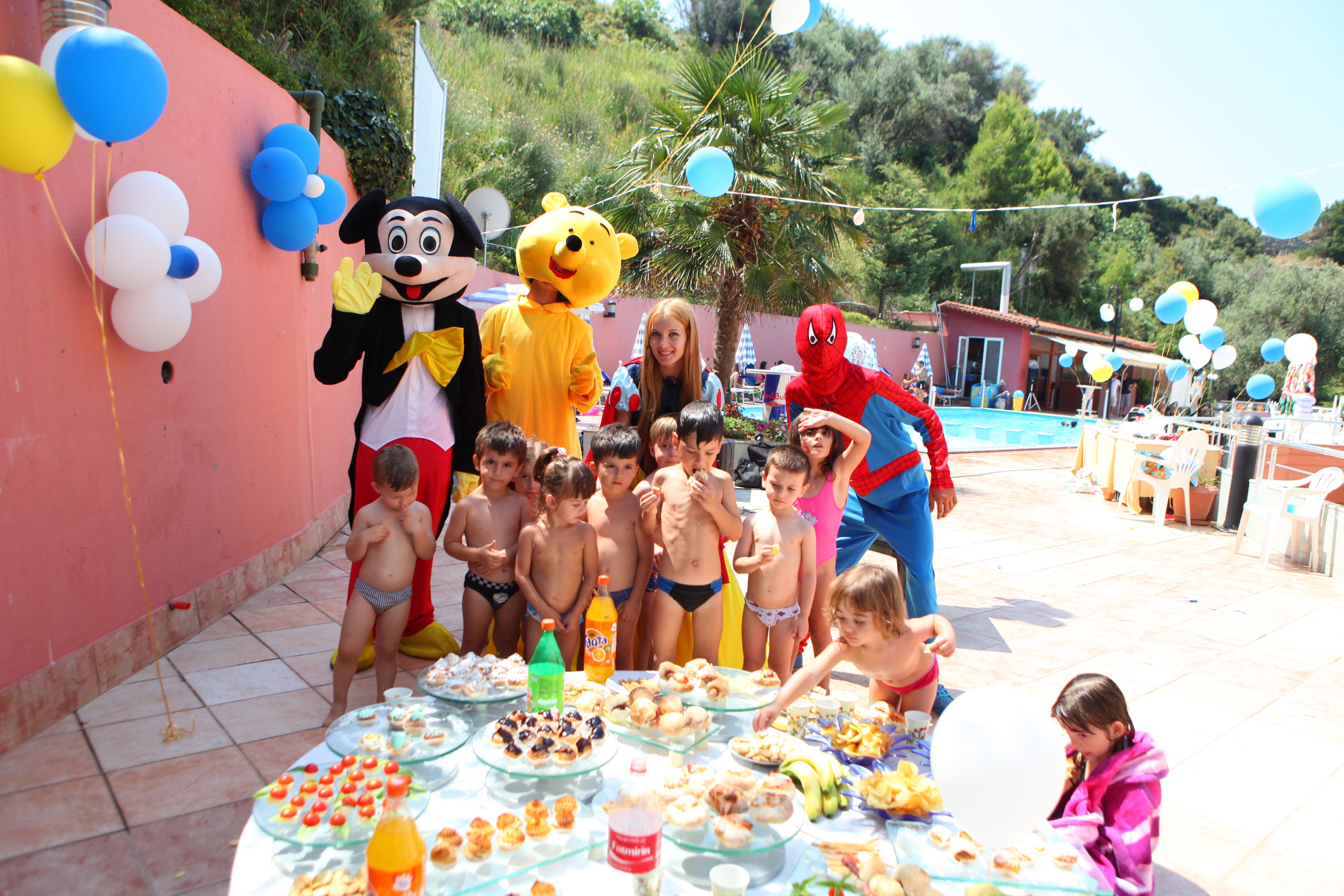 A group of children at a poolside party with food and balloons.