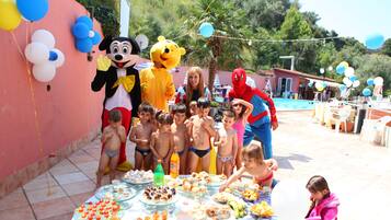 A group of children at a poolside party with food and balloons.