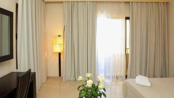 A hotel room with a bed, a desk, a lamp, and a window with curtains.