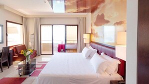 A hotel room with a large bed, a sofa, a desk, and a balcony with a view.