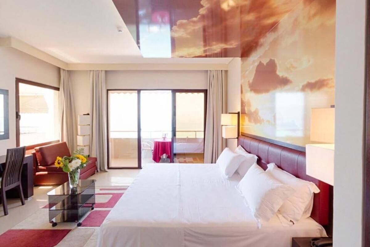 Habitación de hotel con una cama grande, un sofá, un escritorio y un balcón con vistas.