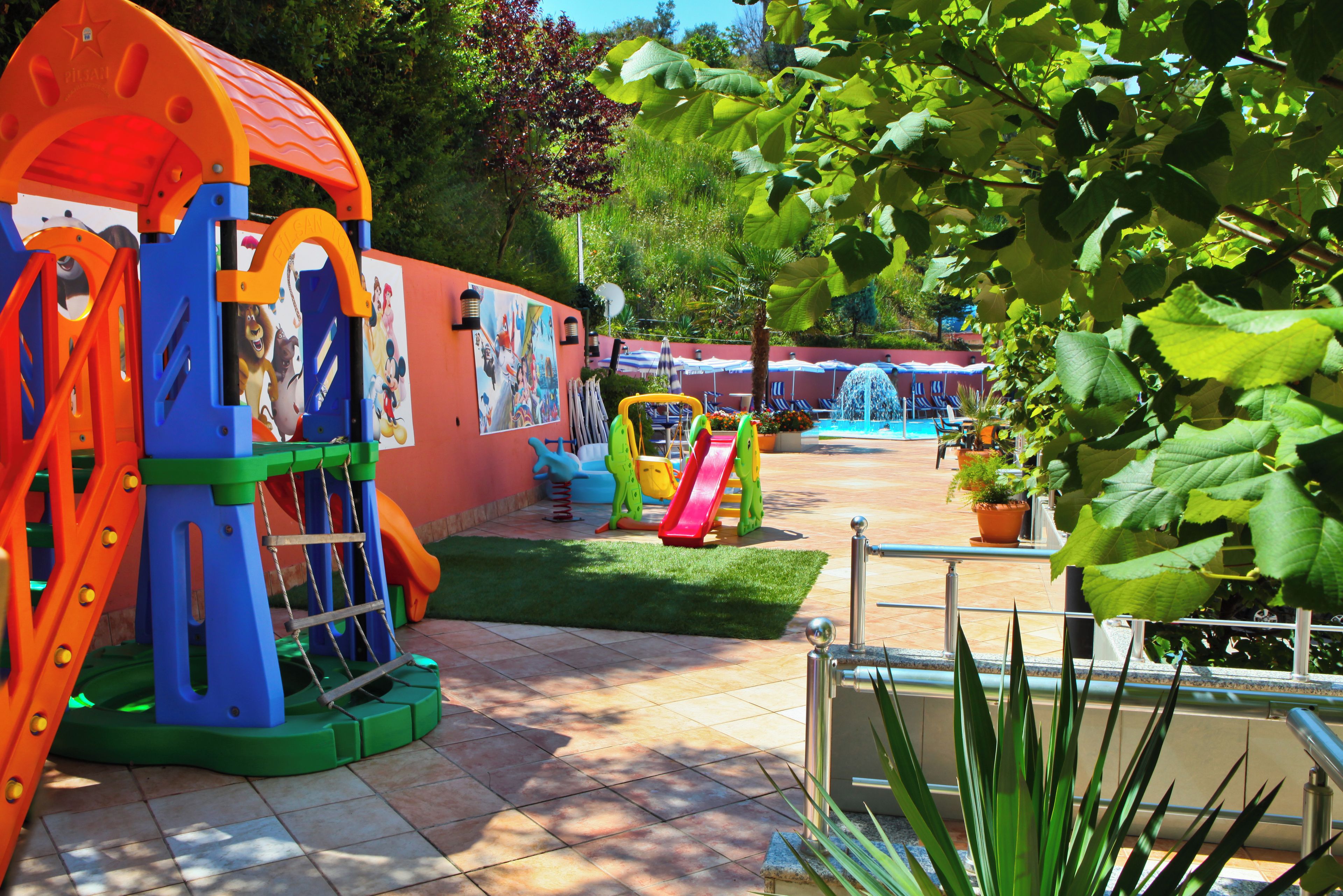 A children's play area with various play structures, a mural, and a pool with lounge chairs.
