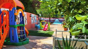 A children's play area with various play structures, a mural, and a pool with lounge chairs.