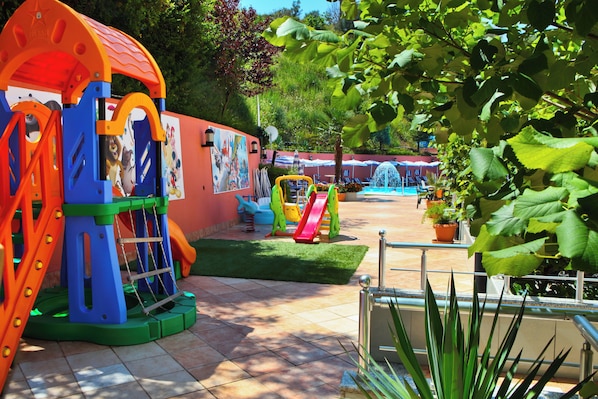 A children's play area with various play structures, a mural, and a pool with lounge chairs.