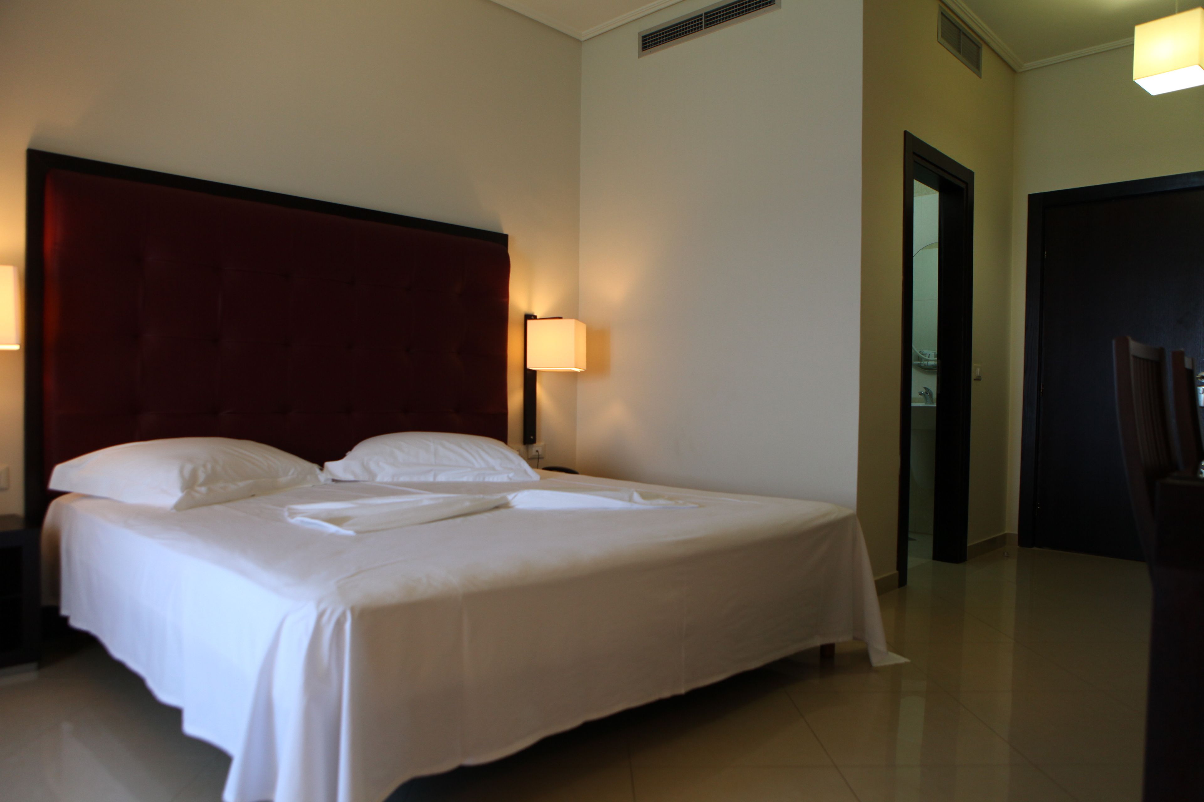A neatly made bed with white linens and a red headboard in a hotel room.