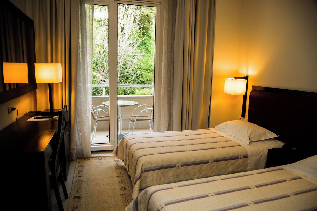 Habitación de hotel con dos camas, un escritorio y una silla. Tiene un balcón con vistas a zonas verdes.