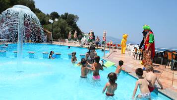 A swimming pool with children and adults, some in costumes, and a water fountain feature.