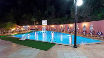 A swimming pool with a fountain, surrounded by lounge chairs and umbrellas, with a signboard in the background.