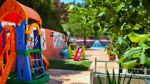 A playground with slides and climbing structures, surrounded by potted plants and a tiled patio area.