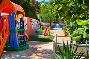 A playground with slides and climbing structures, surrounded by potted plants and a tiled patio area. - New York (Vlorë)
